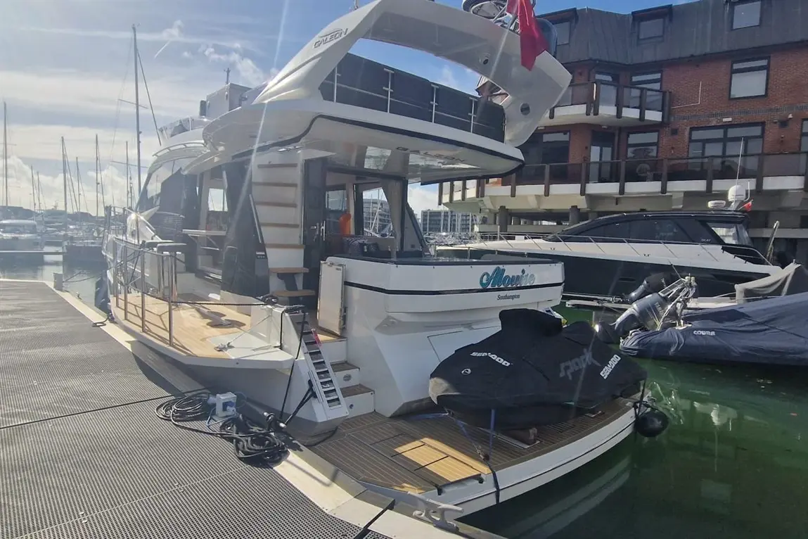 A luxury boat named "Alovice" docked in a marina with yachts, wooden deck, and a scenic waterfront view in Southampton.